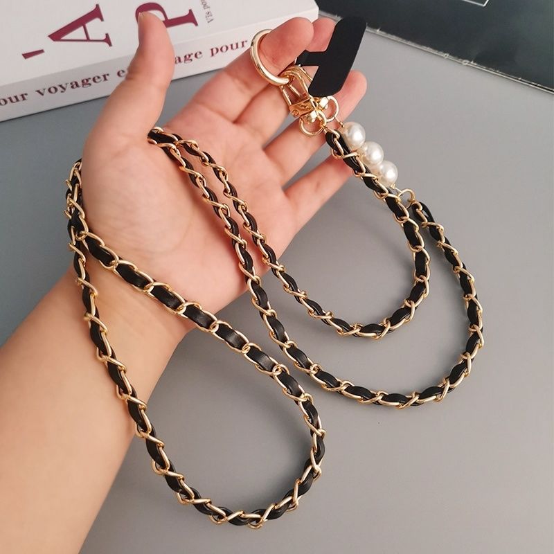 Hand holding a black and gold chain strap with pearls against a gray background