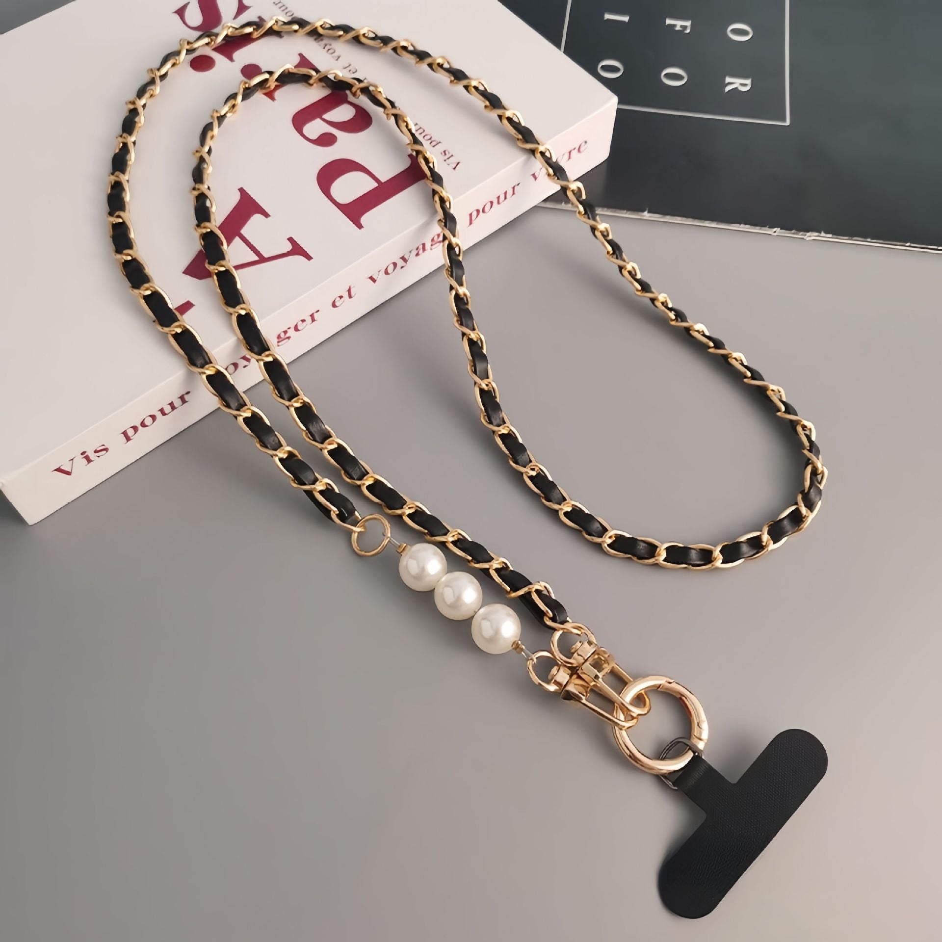 Necklace with black and gold chain and pearl accents on a gray surface