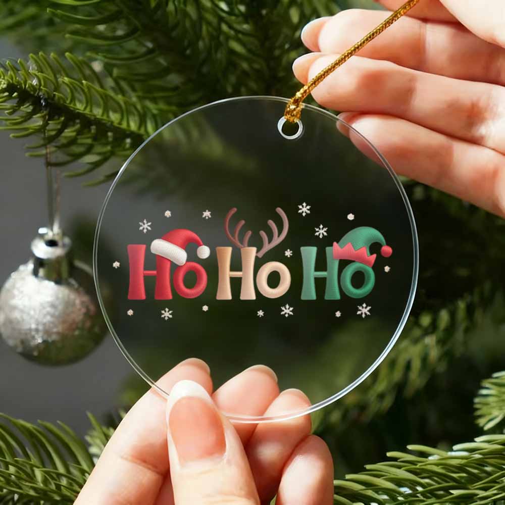 Clear Christmas ornament with 'Ho Ho Ho' text and festive designs held by a hand against a Christmas tree background.