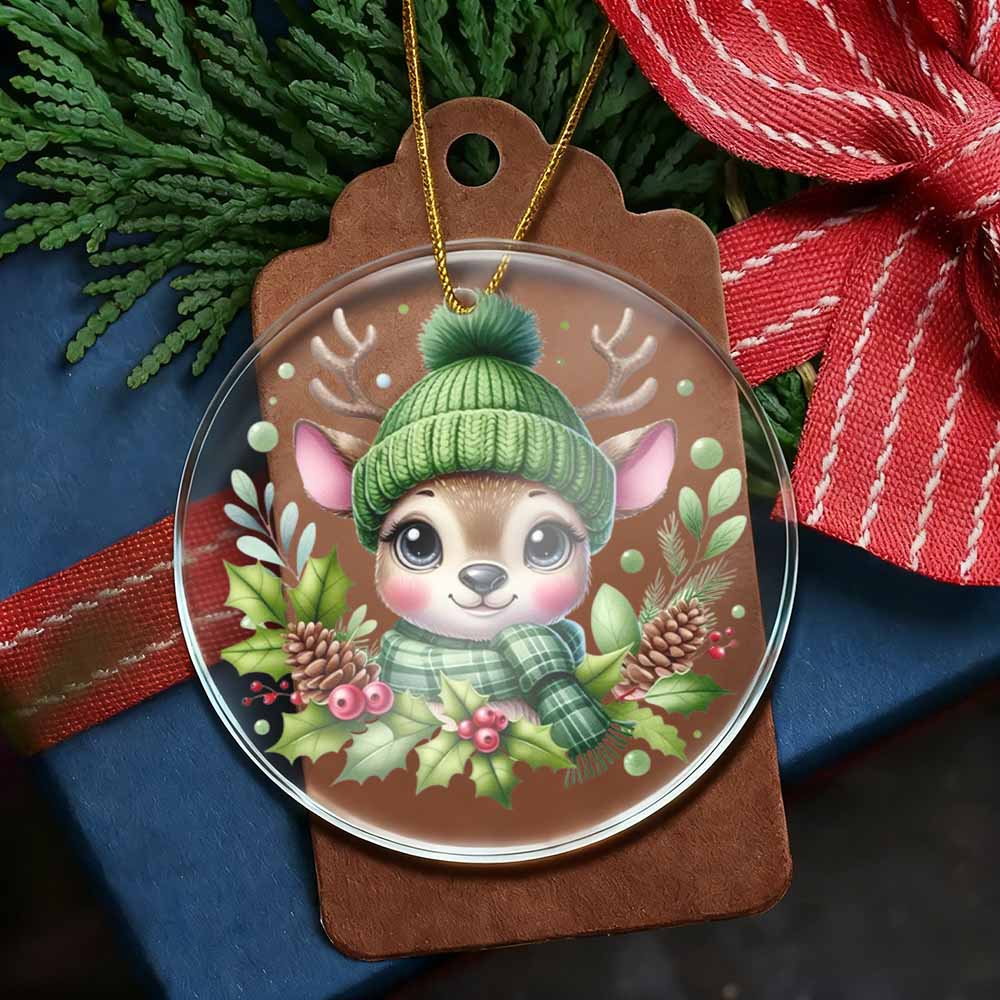 Christmas ornament with a deer wearing a green hat and scarf on a brown tag, surrounded by greenery and ribbons.