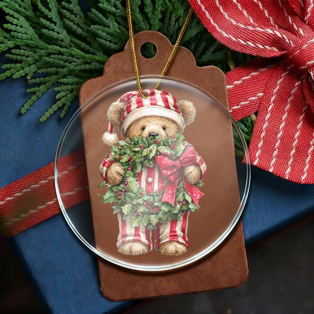 Christmas ornament with a teddy bear holding a wreath on a brown tag, surrounded by greenery and ribbons.