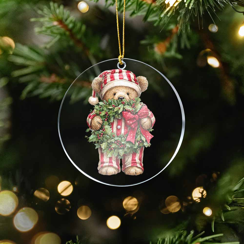 Christmas ornament of a teddy bear holding a wreath on a tree with lights in the background