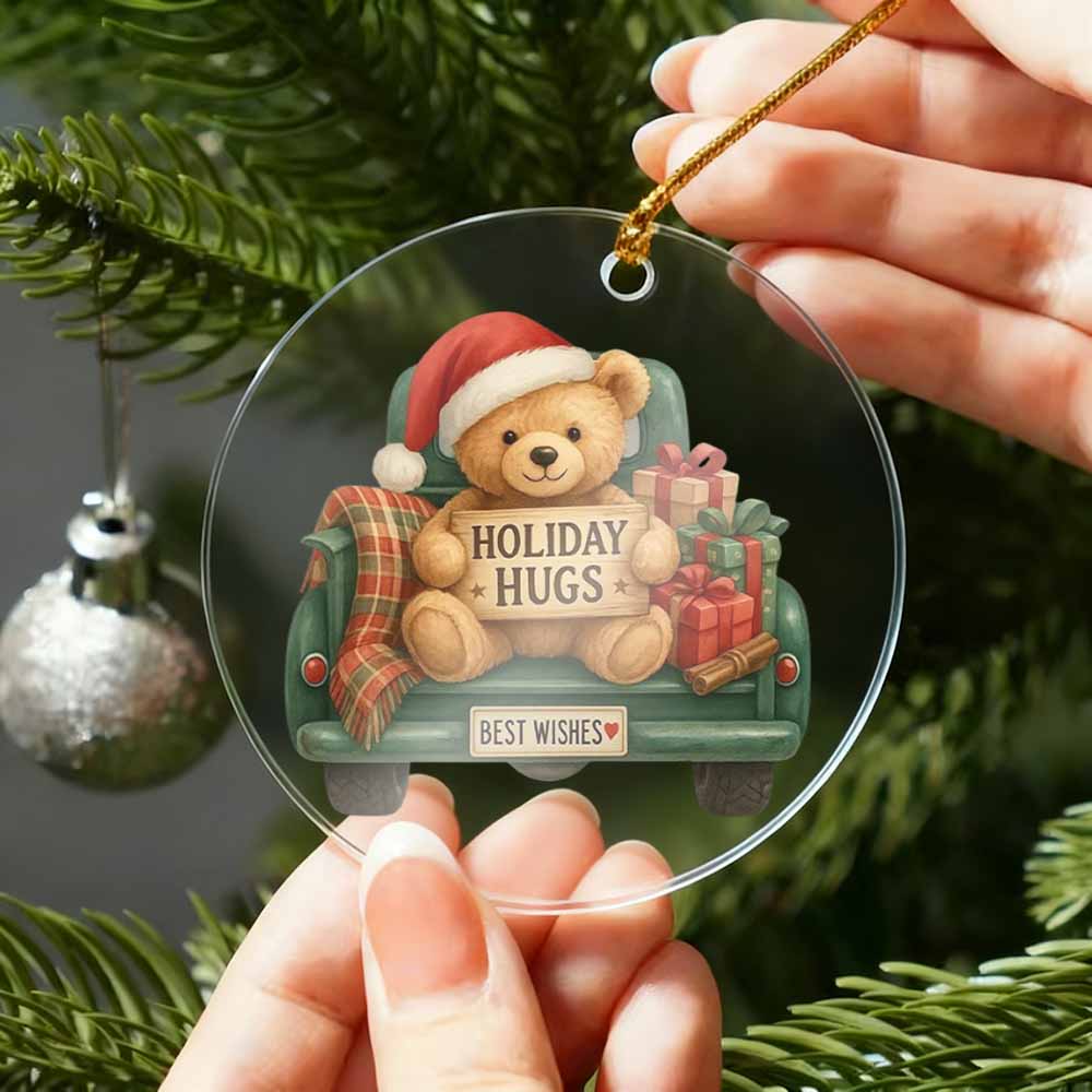Decorative Christmas ornament with a teddy bear and 'Holiday Hugs' text, held by hands against a Christmas tree background.