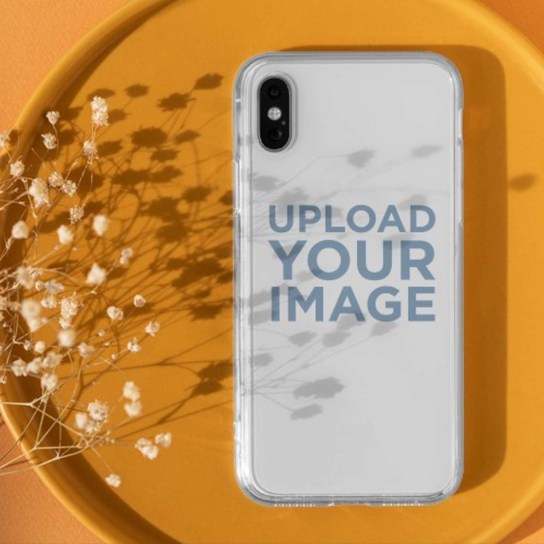 Clear phone case with 'Upload Your Image' text on a yellow surface with dried flowers.